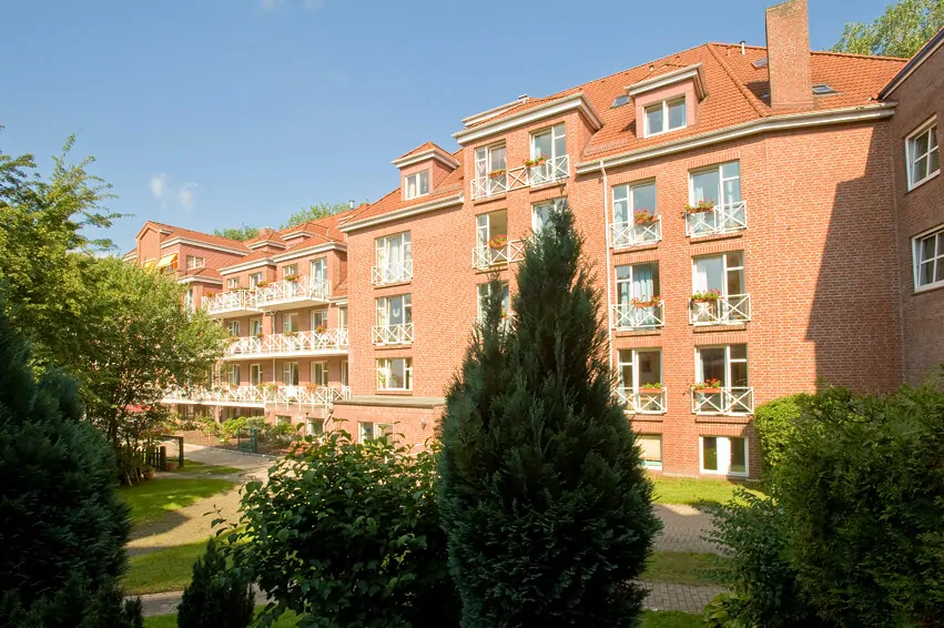 Außenansicht eines Seniorenpflegeheims mit Backsteinfassade, Balkonen und Gartenanlage